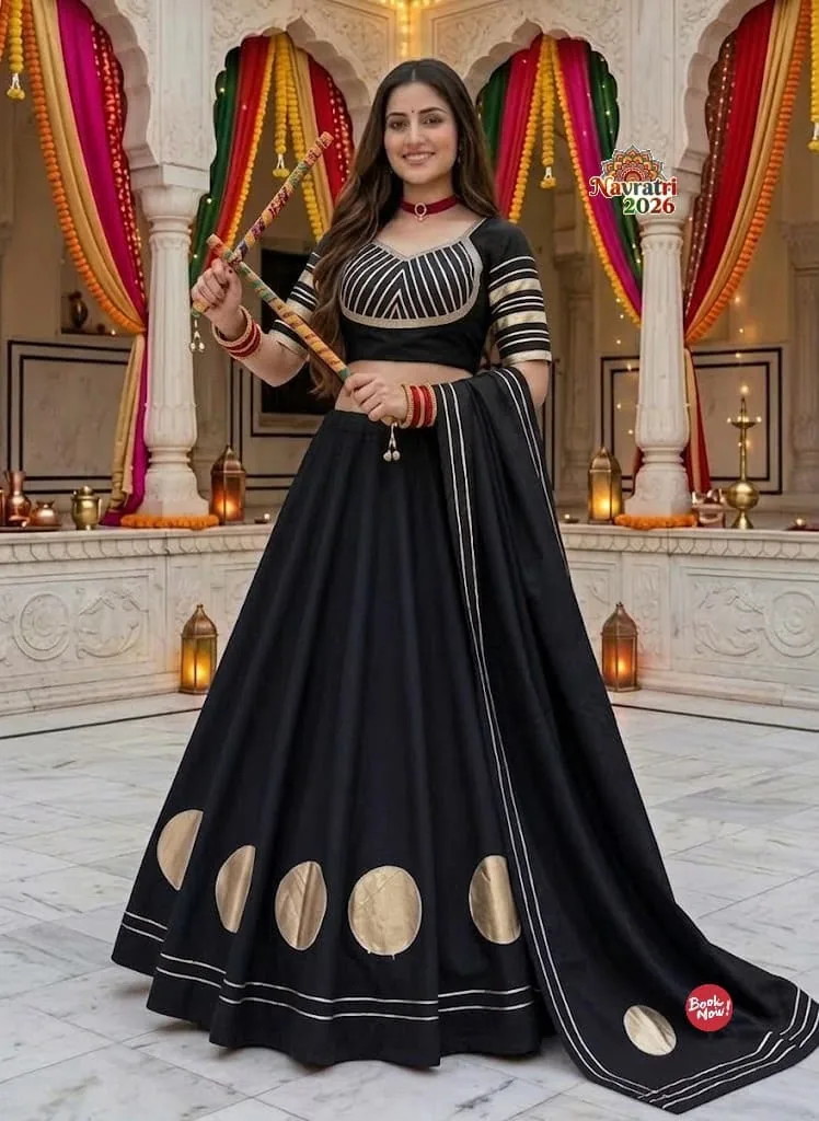 Model in a black lehenga with gold circle motifs, holding dandiya sticks