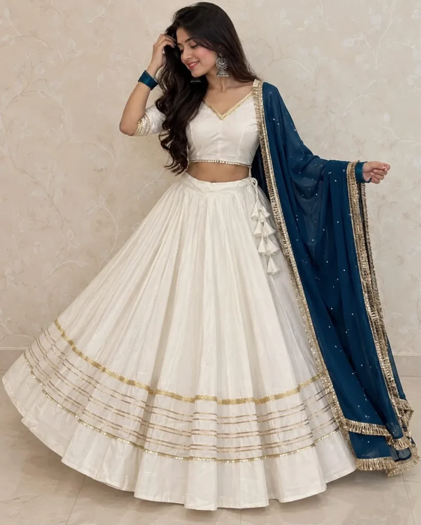 Model in an ivory lehenga with gold stripe detailing and a teal dupatta